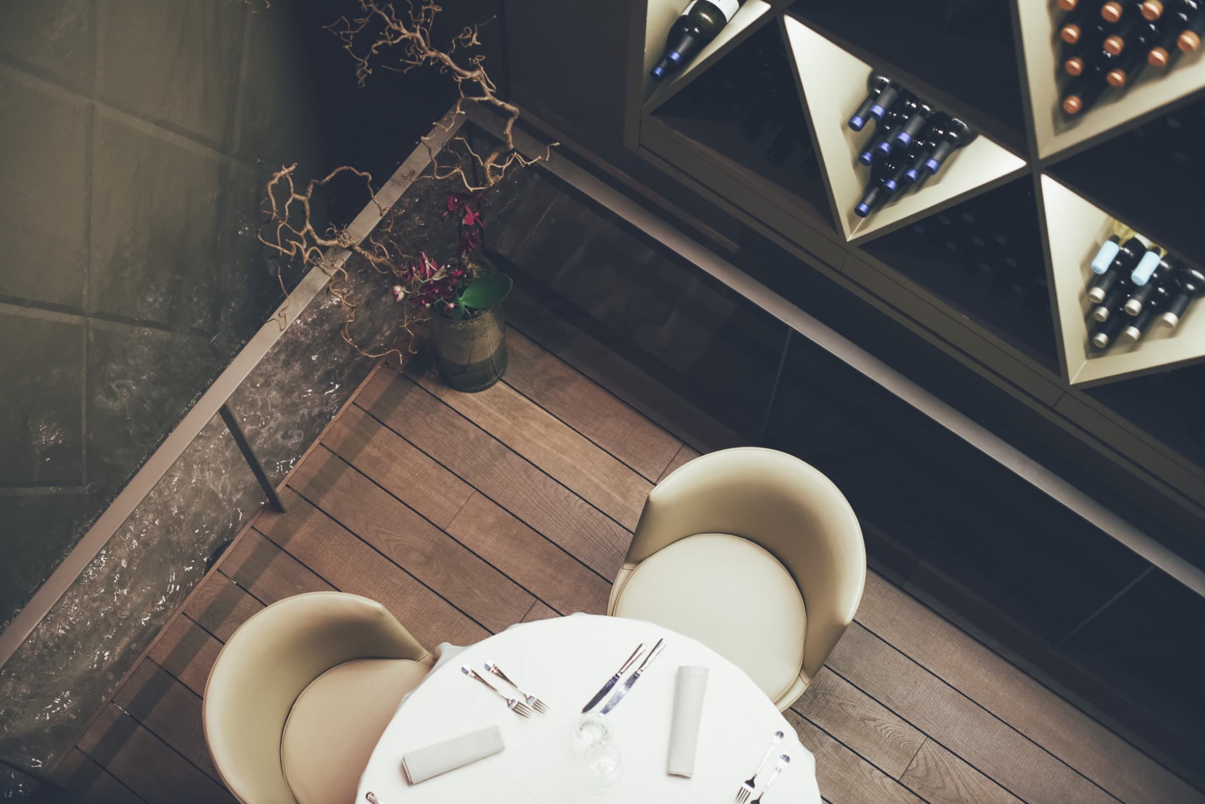 Overhead view of a laid restaurant table beside a lit wine rack.